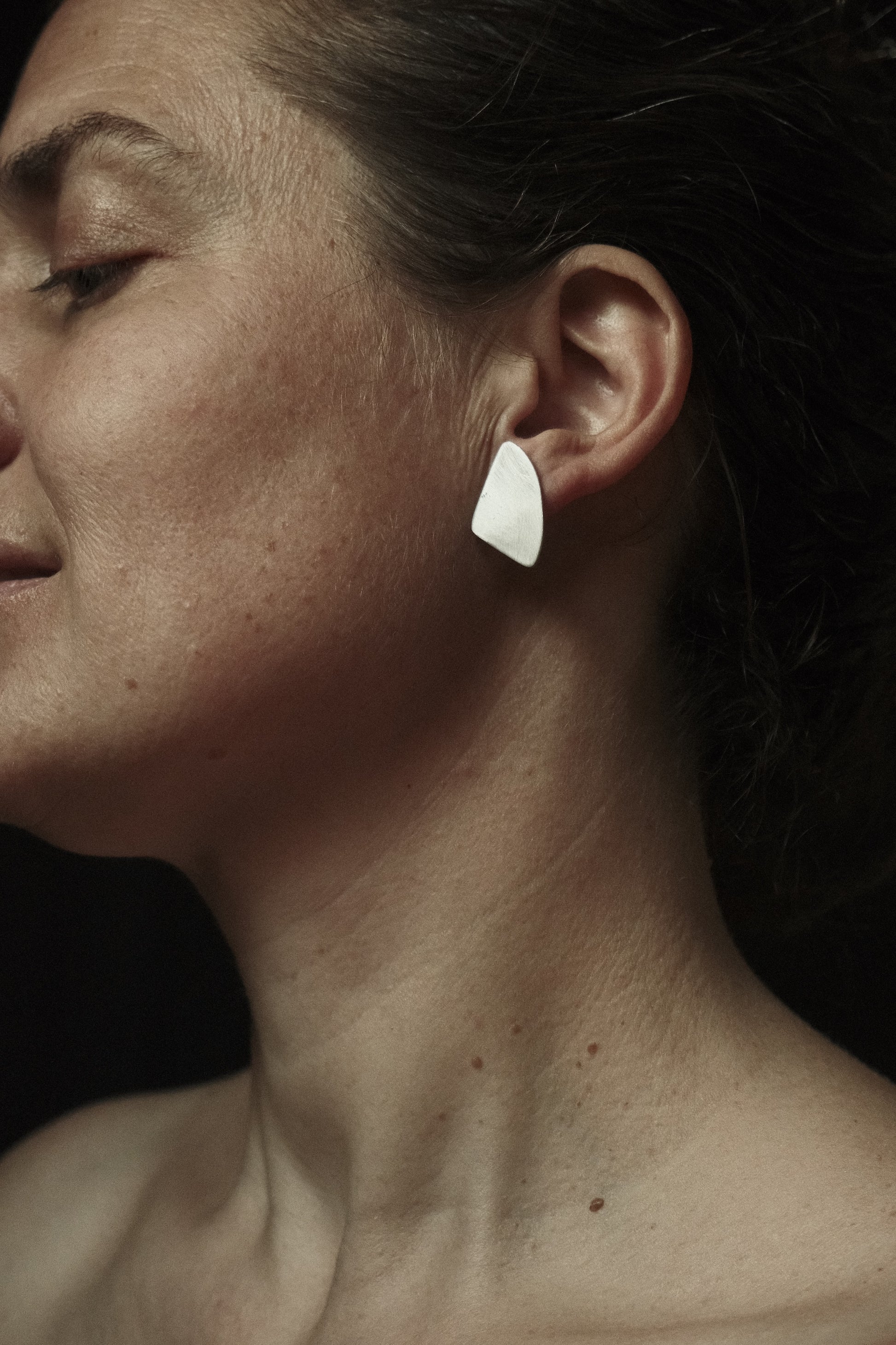 Boucles d’oreilles de petites taille, fixées directement sur le lobe en forme de quart de cercle stylisé. Couleur argenté, effet brossé.