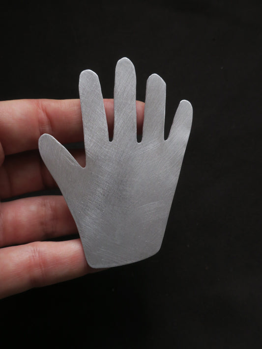 Broche volumineuse en forme de main. Forme naïve et aspect argenté.