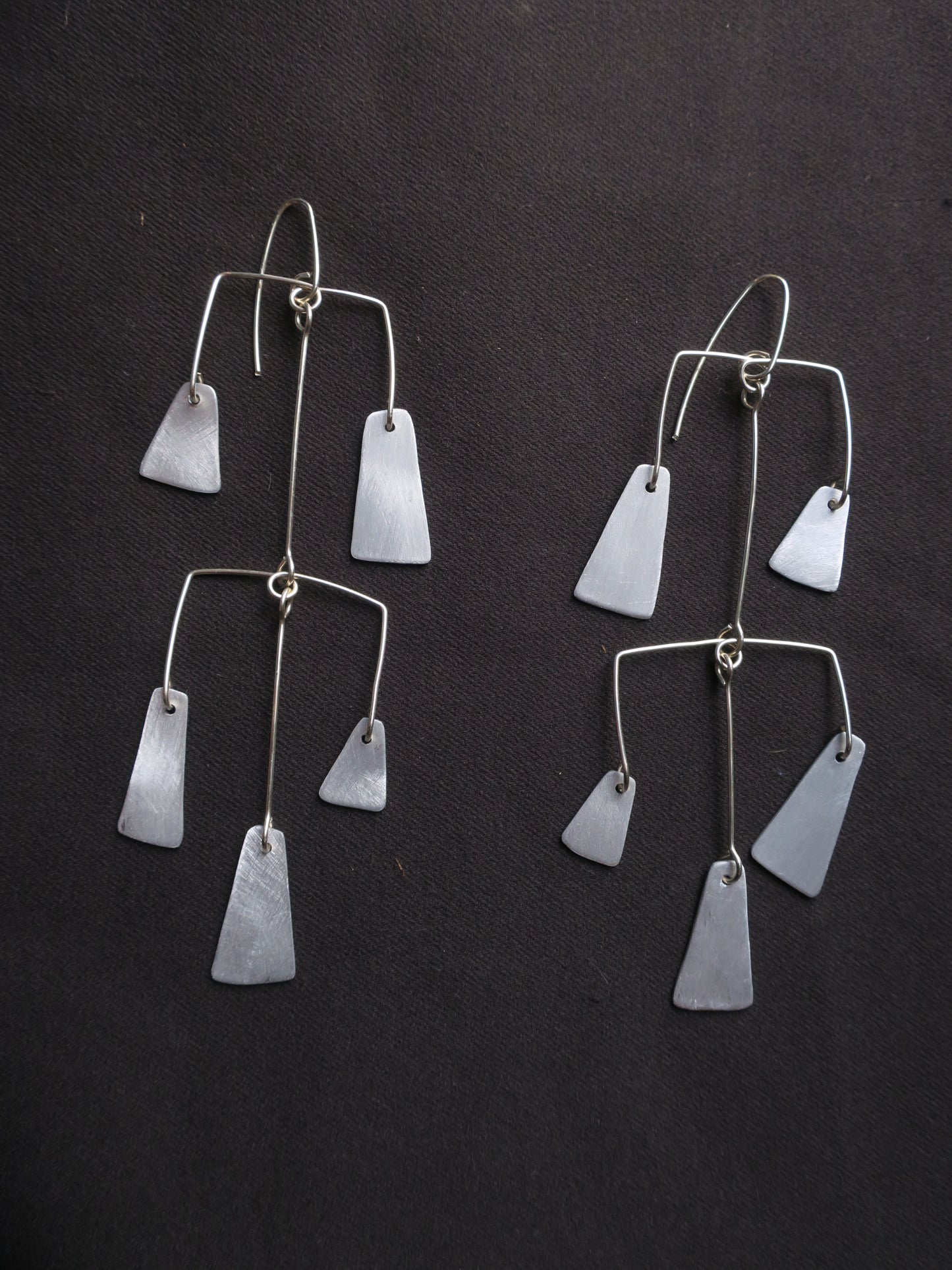 boucles d’oreilles multipièces façonnées en fil d’argent et en aluminium, comme des petites mobils évoquant les carillons traditionnels constitués de multiples cloches et clochettes. L’ensemble est articulé pour donner du mouvement à ce bijou.