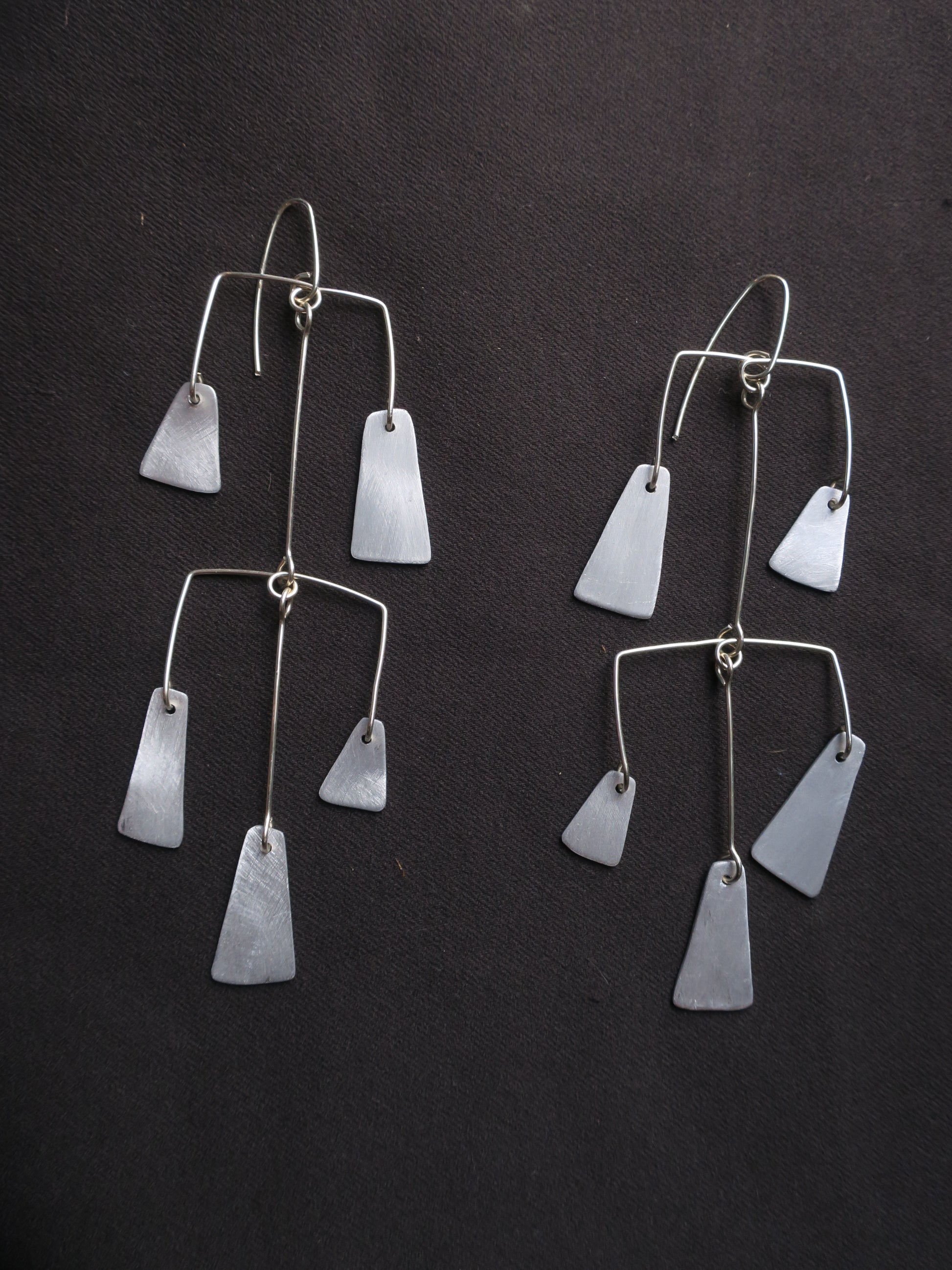 boucles d’oreilles multipièces façonnées en fil d’argent et en aluminium, comme des petites mobils évoquant les carillons traditionnels constitués de multiples cloches et clochettes. L’ensemble est articulé pour donner du mouvement à ce bijou.