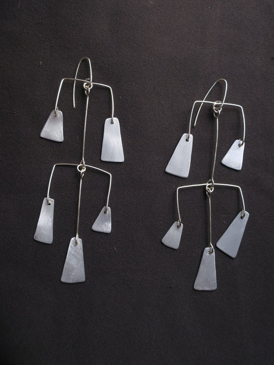 boucles d’oreilles multipièces façonnées en fil d’argent et en aluminium, comme des petites mobils évoquant les carillons traditionnels constitués de multiples cloches et clochettes. L’ensemble est articulé pour donner du mouvement à ce bijou.