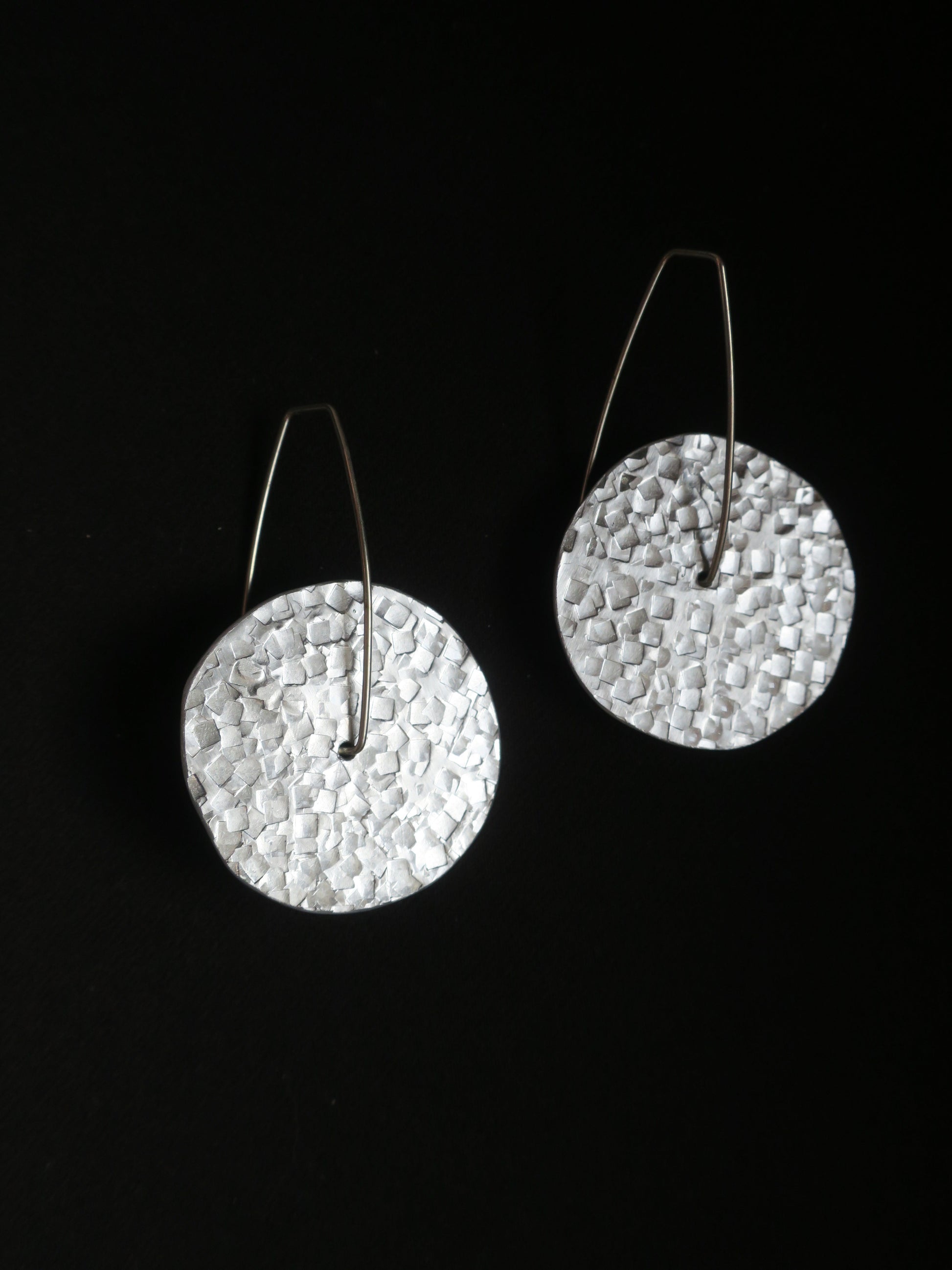 Boucles d’oreilles rondes montées sur une tige en argent 925 donnant un aspect mobile au bijou. Rond argenté en aluminium martelé.