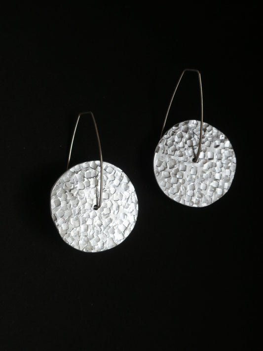 Boucles d’oreilles rondes montées sur une tige en argent 925 donnant un aspect mobile au bijou. Rond argenté en aluminium martelé.