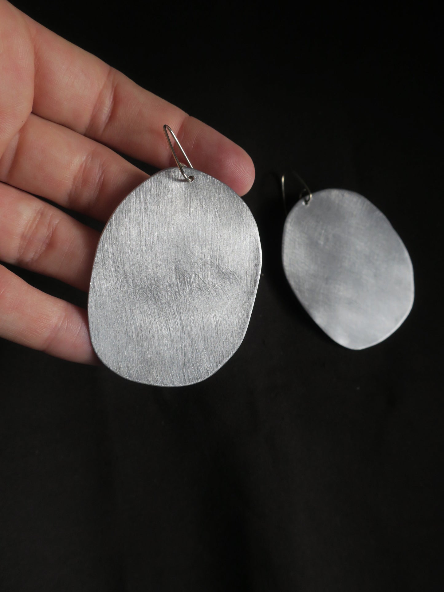 boucles d’oreilles imposantes, rondes et irrégulières de couleur argenté avec un aspect métal brossé.
